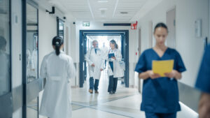 Doctors in white coats and nurses in scrubs walking through a busy modern hospital corridor